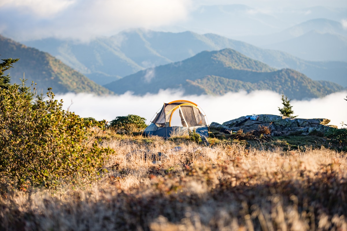 Orange camping tent pitched on mountain top at golden hour with scenic valley view — sleeping bag temperature rating guide India