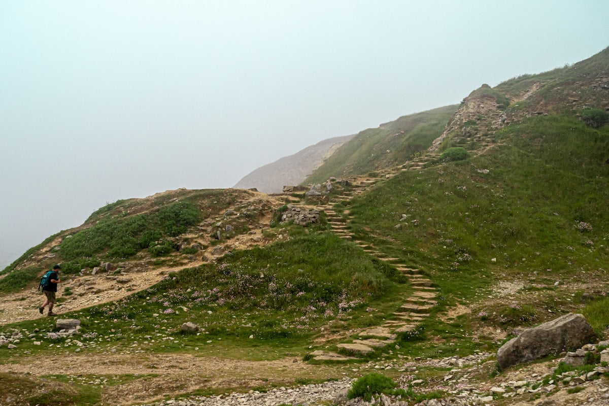 Trekker hiking up stone steps on a lush green misty hillside — complete Sahyadri trek gear list beginner guide